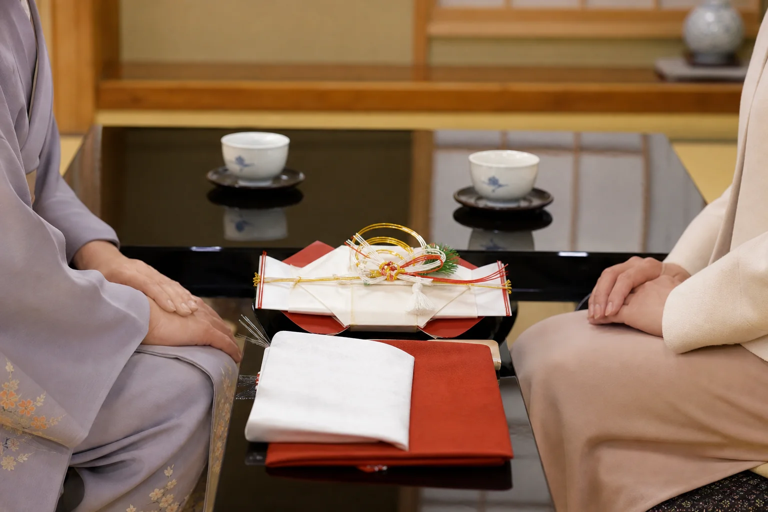 料亭の個室で、訪問着の袖口とワンピースの袖口が座卓の上に並ぶ手元の写真